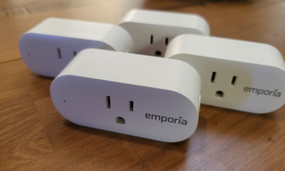 Four Emporia Smart Plugs displayed on a wooden table.