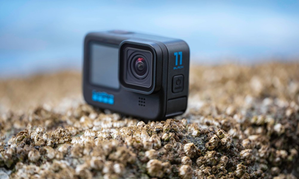 The GoPro Hero 11 Black on a rock with barnacles next to the ocean.