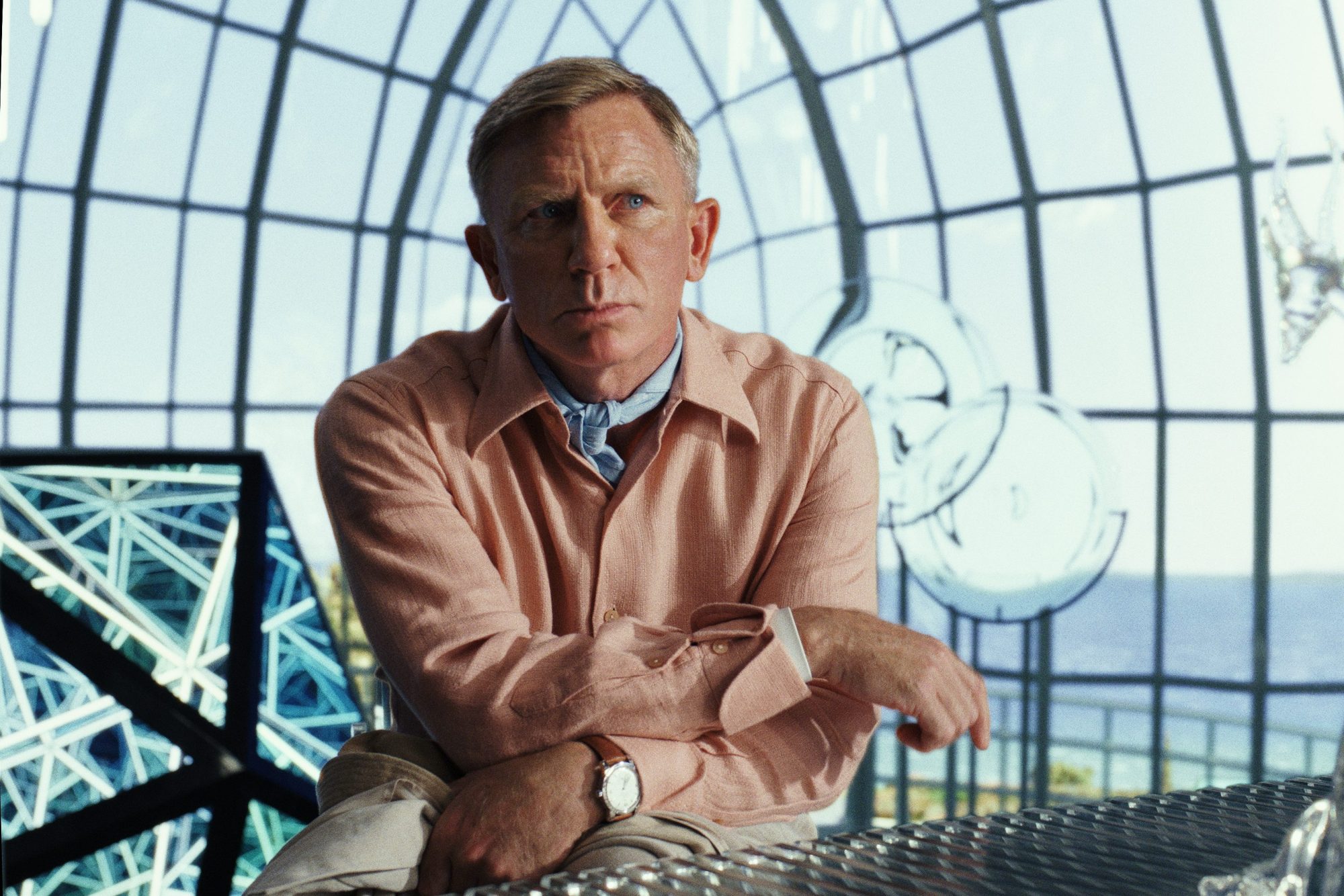 Daniel Craig fica de pé e pondera em uma cena de Glass Onion: A Knives Out Mystery.