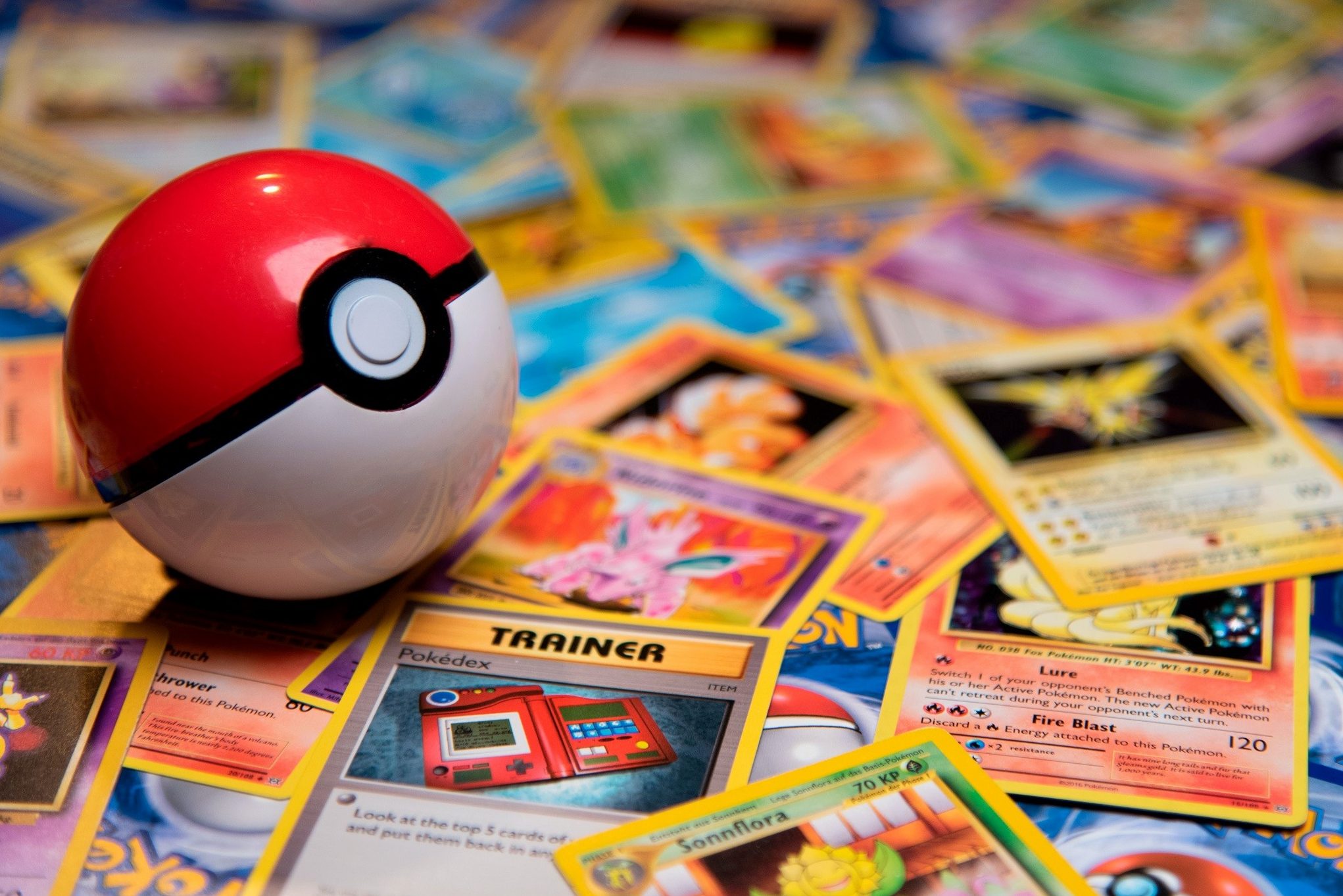 Pokeball on pile of Pokemon Trading Cards in room.