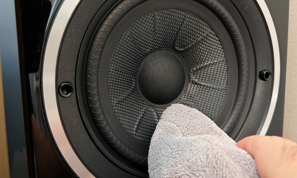 A speaker being wiped with a microfiber cloth.