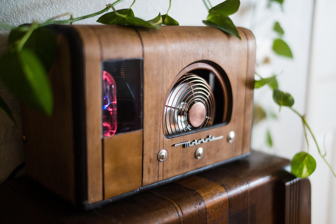 Un pc à l'intérieur d'un boîtier de radio Motorola en bois vintage avec un ventilateur en acier inoxydable à l'avant, entouré de feuilles vertes.