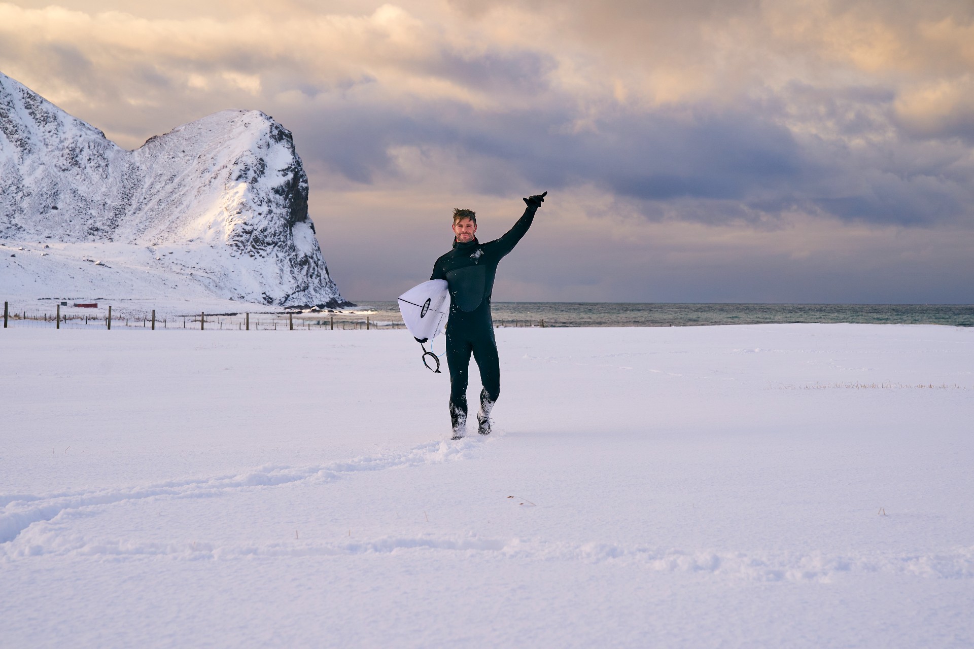 Chris Hemsworth segura uma prancha de surf em um deserto ártico em uma cena de Limitless.