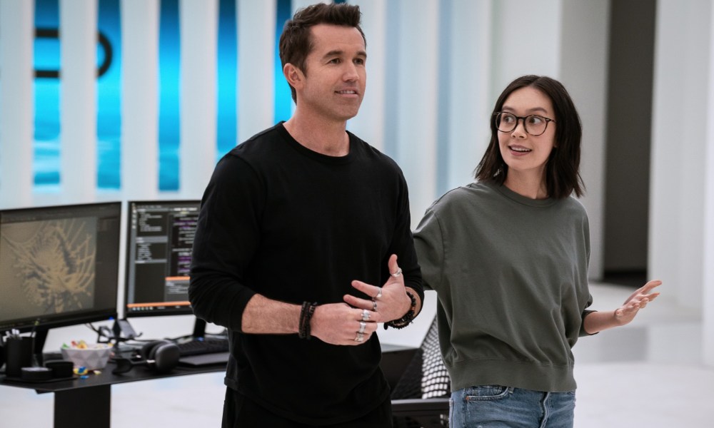 Rob McElhenney and Charlotte Nicdao smile while walking through an office in a scene from season 3 of Mythic Quest.