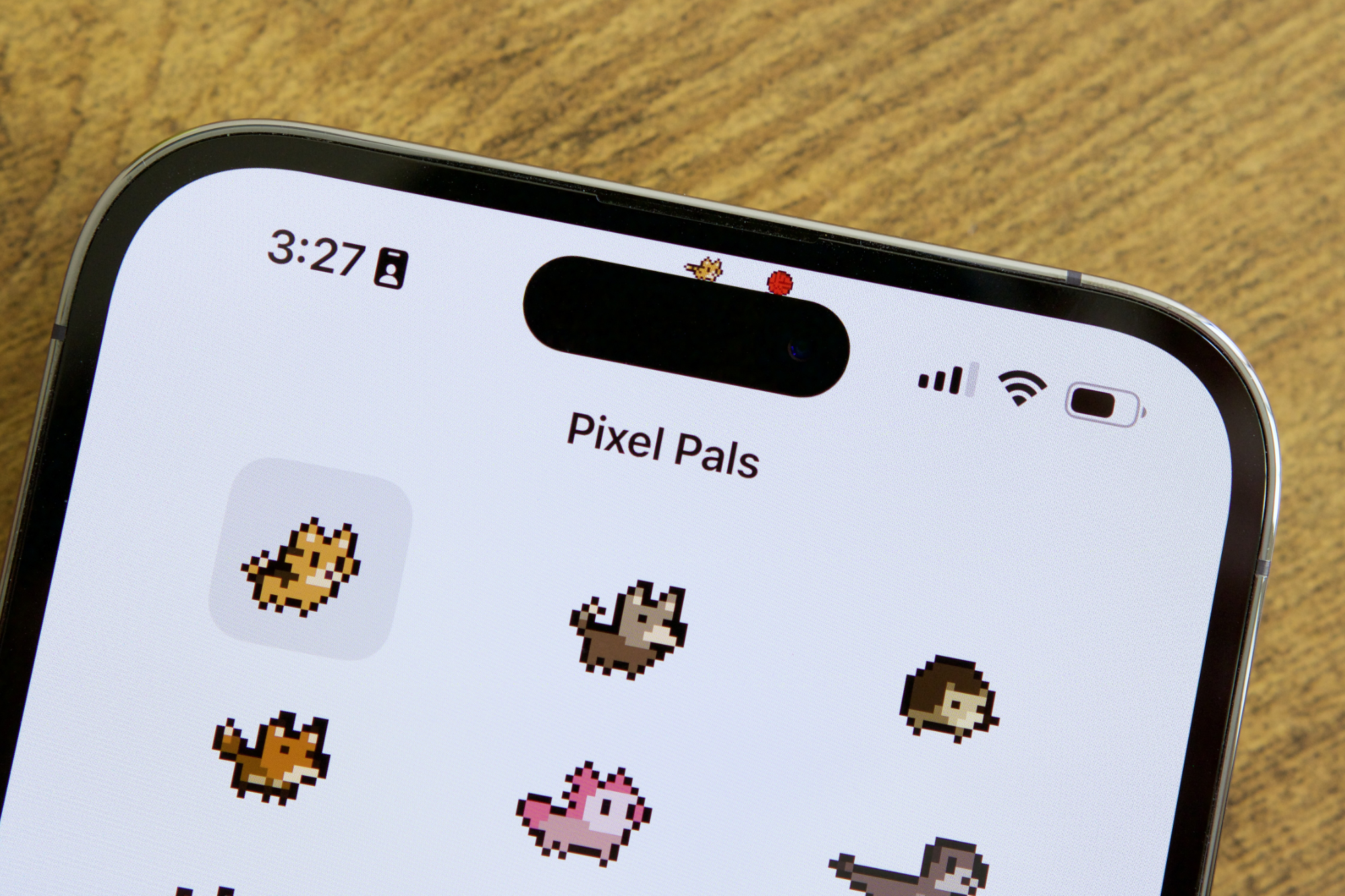 Приложение Pixel Pals на iPhone 14 Pro Max. Цифровой кот гоняется за красным мячиком на вершине Динамического острова.