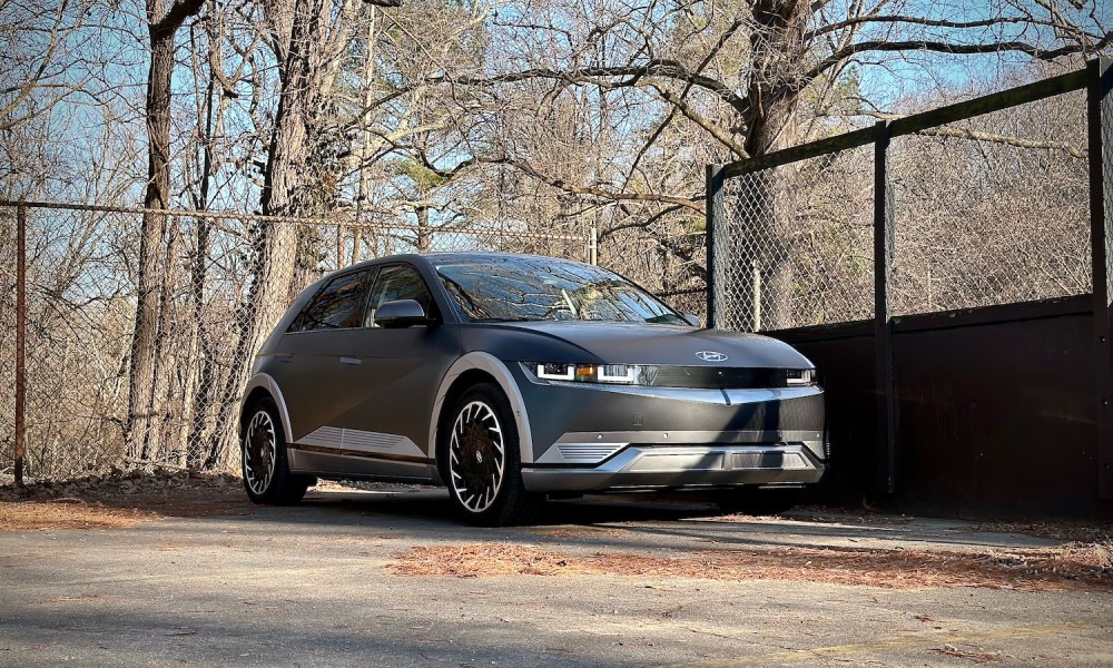 2022 Hyundai Ioniq 5 Limited AWD front end angle from passenger's side in front of a fence with trees in the back.