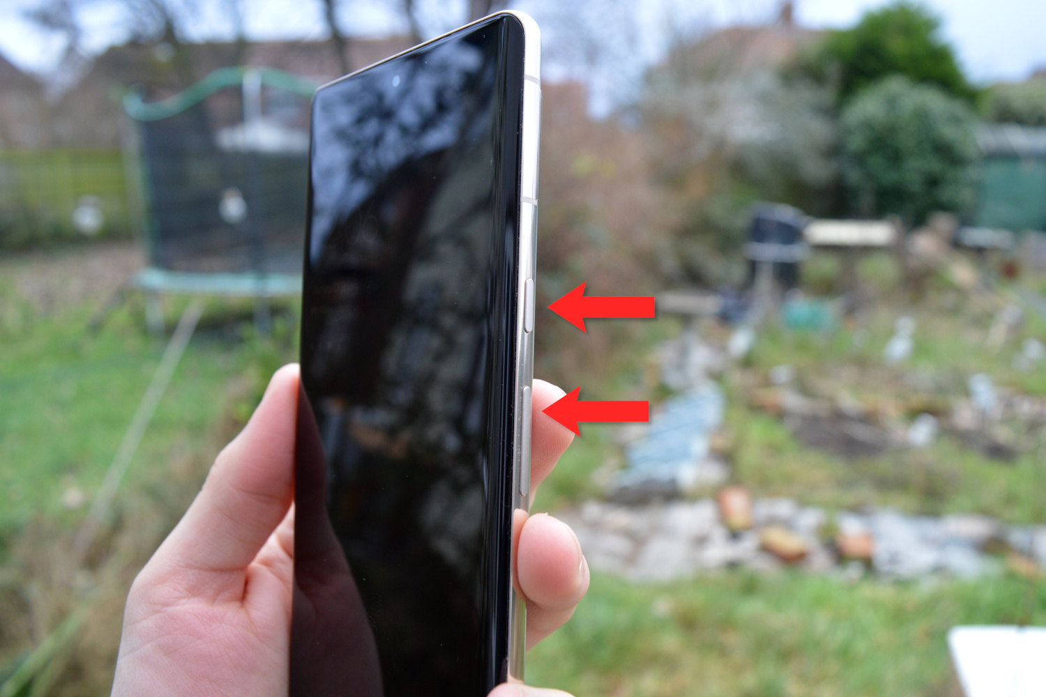 The Pixel 7 Pro outdoors. Red arrows mark the butotns to press to screenshot.