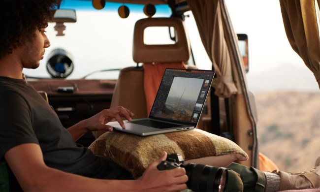 A person sitting in a vehicle using a MacBook Pro on their lap.