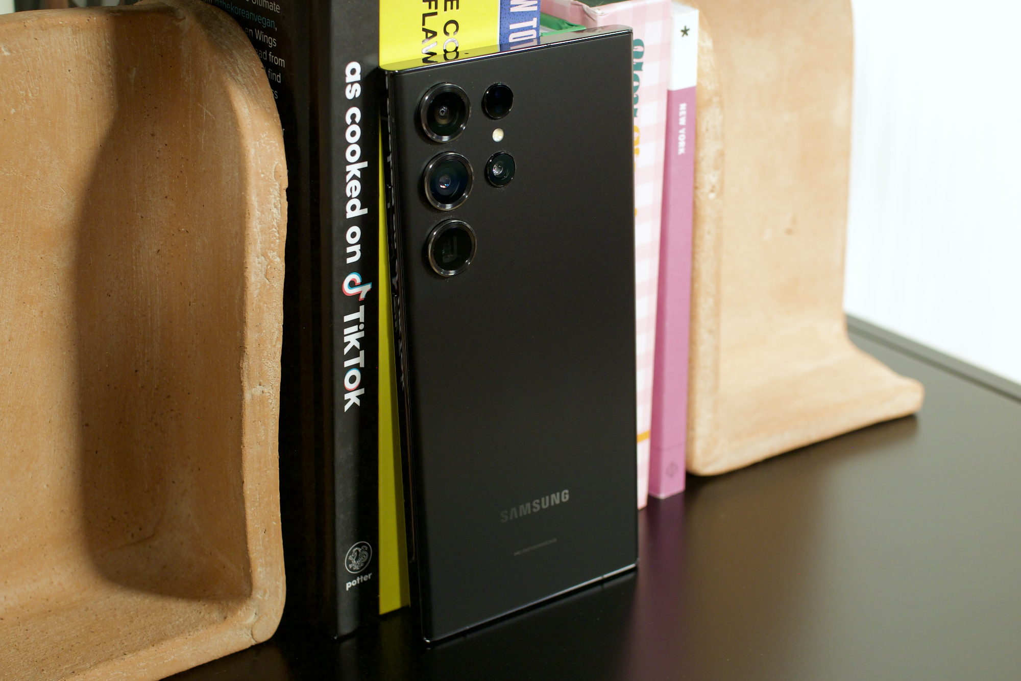 A black Samsung Galaxy S23 Ultra standing up against a row of books.