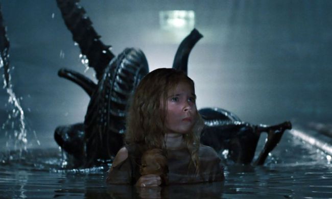 An alien rises up from the water behind Newt in a sewer system.