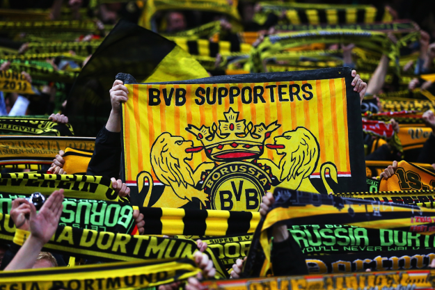 Fans holding Dortmund scarves in the air at a soccer match.