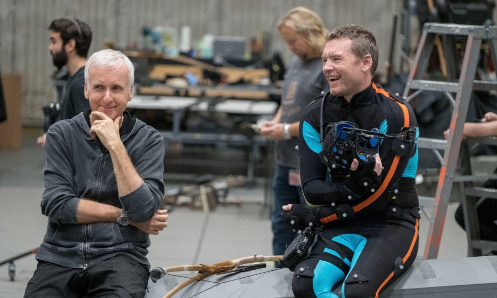 James Cameron sits on the deck of a pool with Sam Worthington while filming Avatar: the Way of Water.