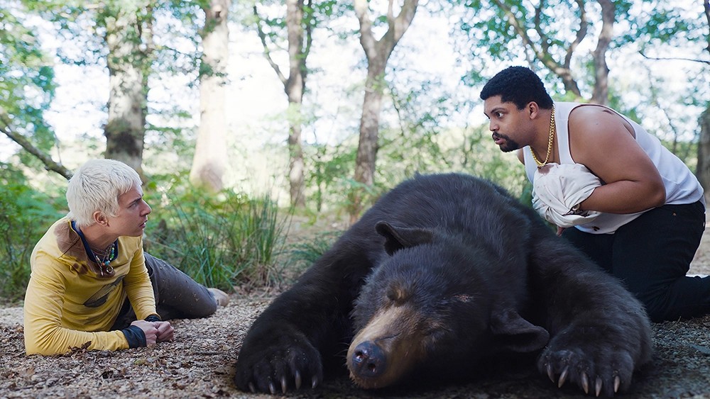 Dois homens pairam sobre um urso desmaiado em Cocaine Bear.