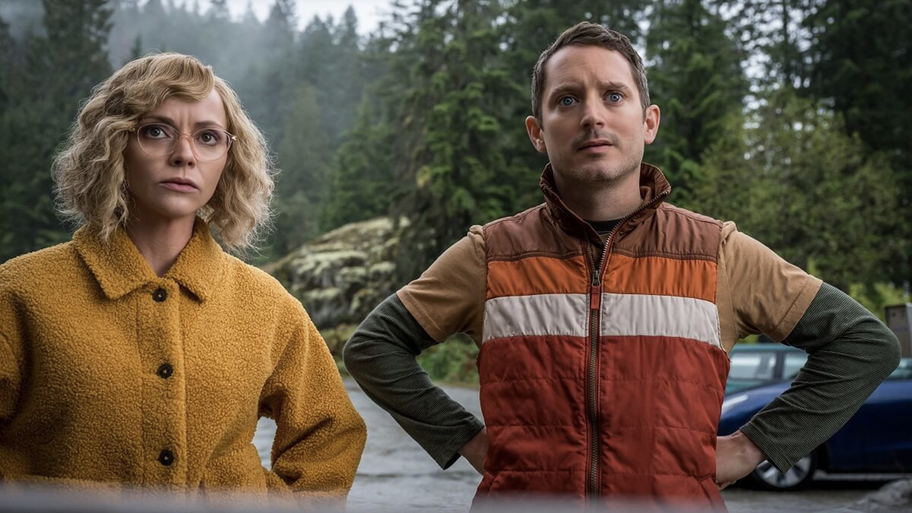 Christina Ricci and Elijah Wood standing with hands on hips looking at something in a scene from Yellowjackets.