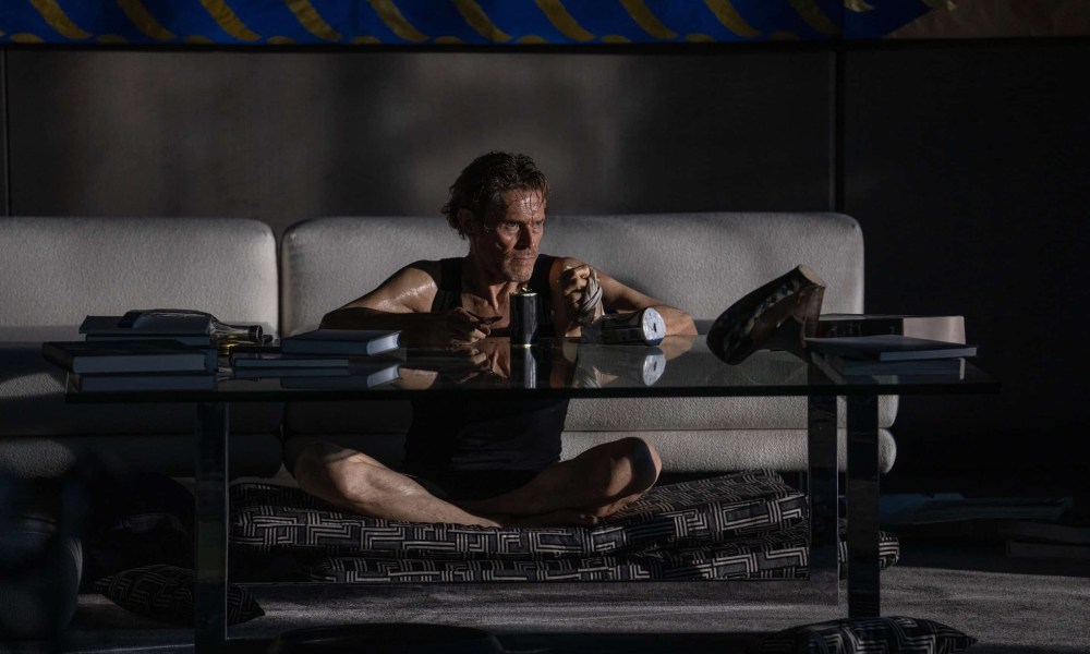 Willem Dafoe sits in front of a table in Inside.