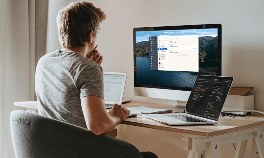 A person using 1Password on a desktop all-in-one computer while sat at a desk. There are two laptops next to them on the desk.