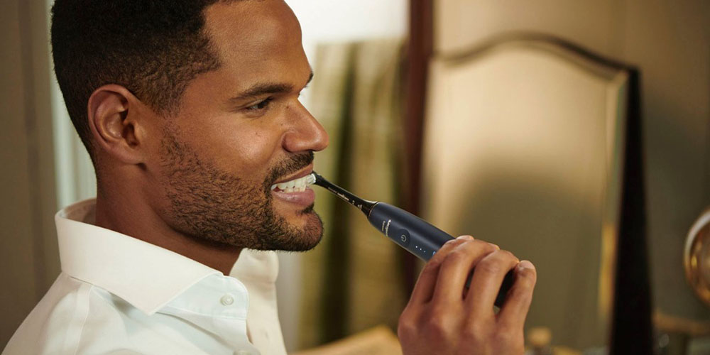 Un hombre usando el cepillo de dientes eléctrico recargable Philips Sonicare 9900 Prestige y sonriendo.