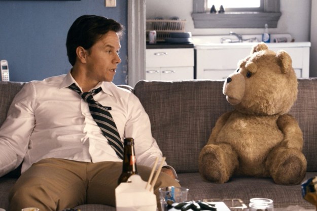 A man sits down on the couch with his teddy bear.