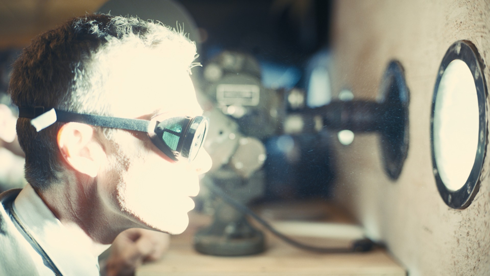 Cillian Murphy stares through a small window at an atomic blast, his face illuminated by light.