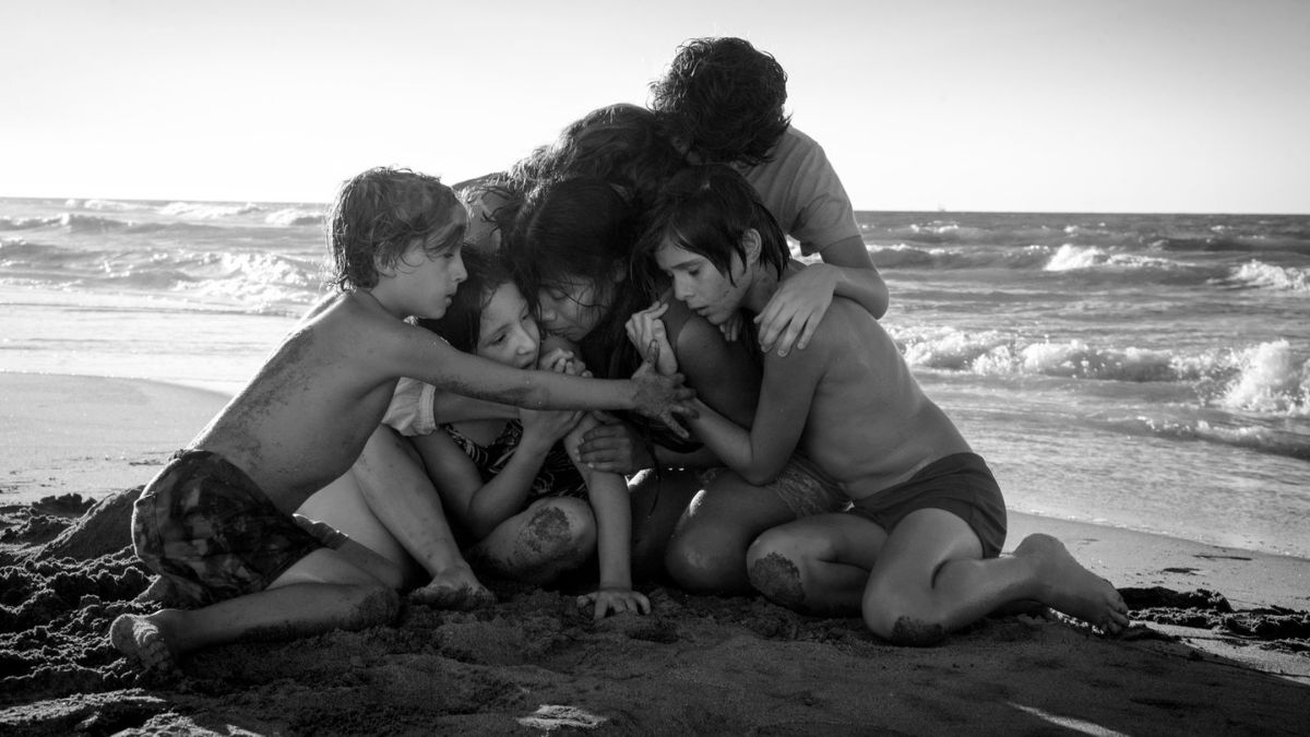 Um grupo de crianças e duas mulheres se abraçando na praia do filme Roma.