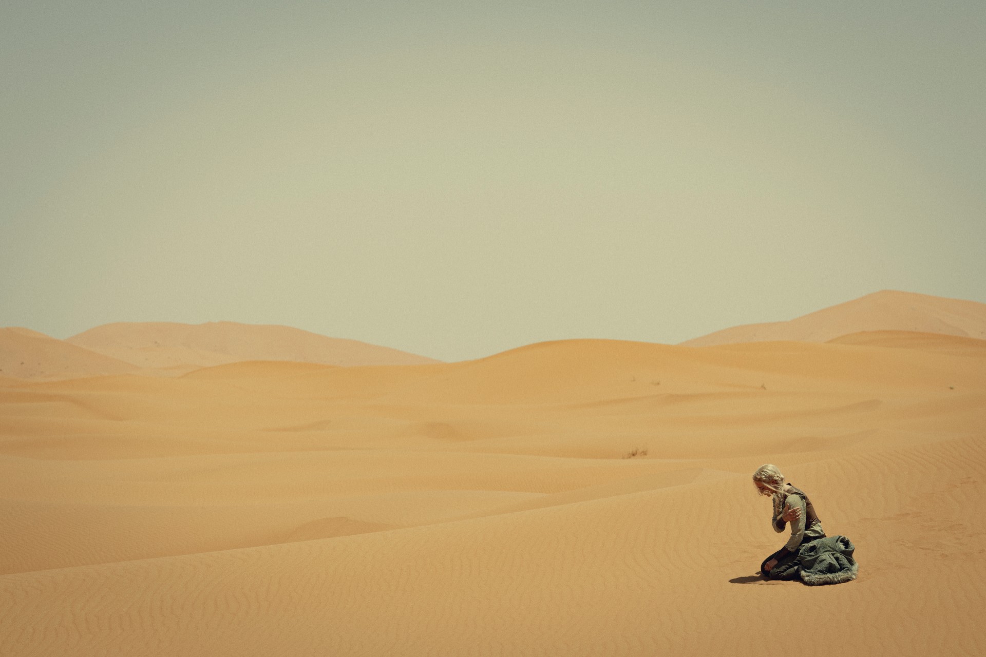 A woman sits in a vast desert in The Witcher season 3.