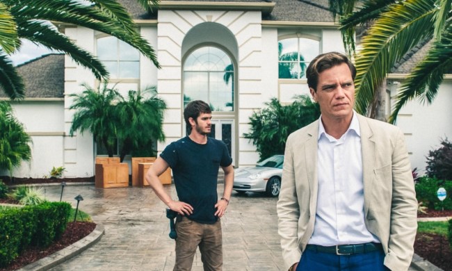 Andrew Garfield stands behind Michael Shannon in front of a house in 99 Homes.