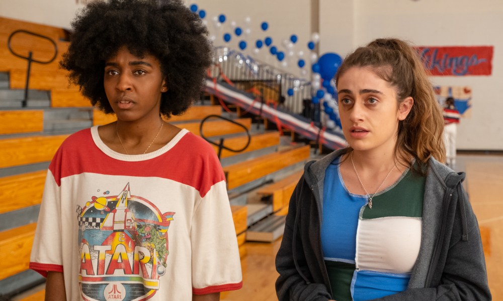 Ayo Edebiri and Rachel Sennott stand near a set of gym bleachers in Bottoms.