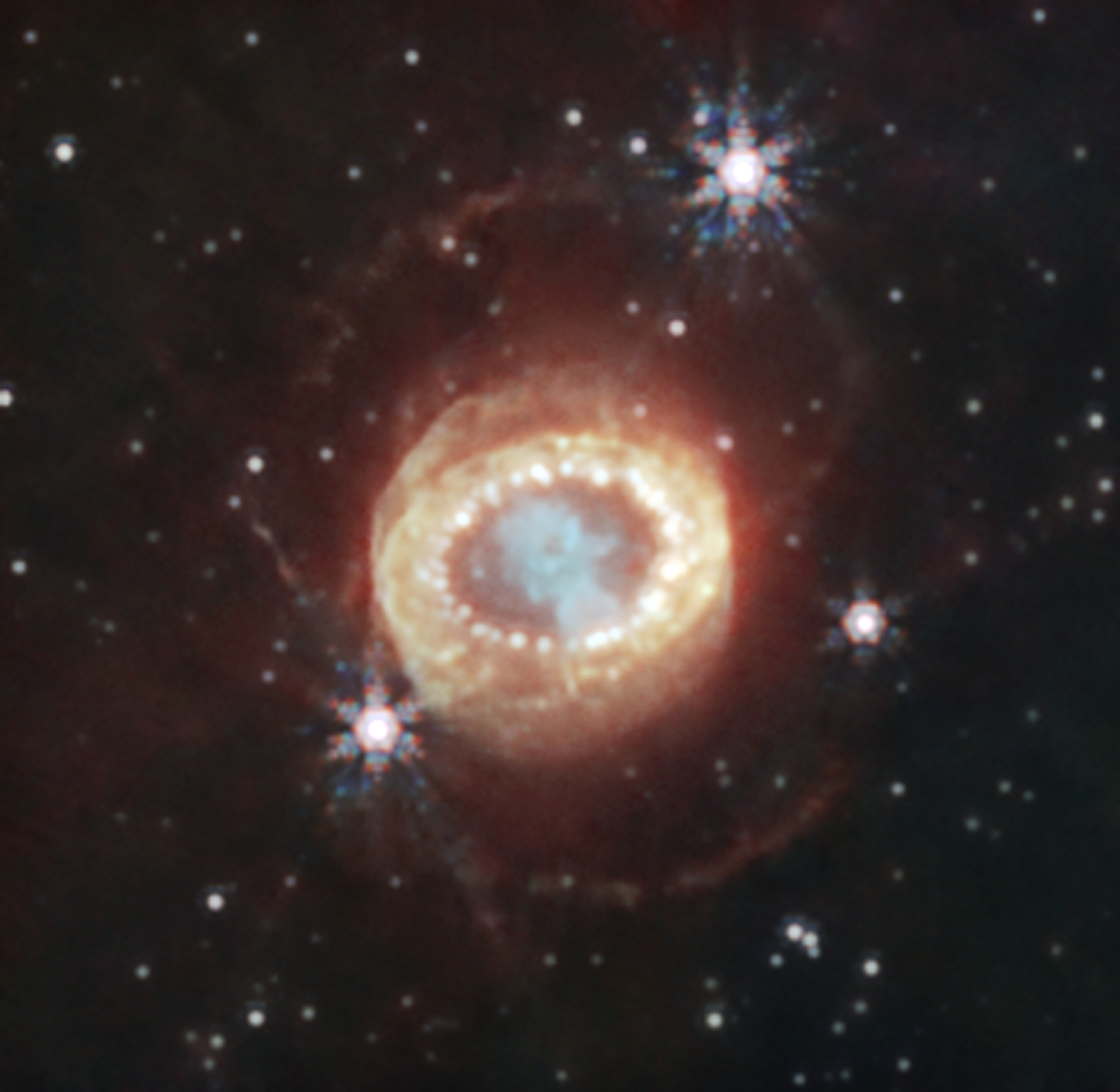 La NIRCam (Near-Infrared Camera) de Webb a capturé cette image détaillée de SN 1987A (Supernova 1987A). Au centre, la matière éjectée de la supernova forme un trou de serrure. Juste à gauche et à droite se trouvent de faibles croissants récemment découverts par Webb. Au-delà d'eux, un anneau équatorial, formé de matériaux éjectés des dizaines de milliers d'années avant l'explosion de la supernova, contient des points chauds brillants. À l’extérieur se trouvent une émission diffuse et deux anneaux extérieurs faibles. Dans cette image, le bleu représente la lumière à 1,5 microns (F150W), le cyan à 1,64 et 2,0 microns (F164N, F200W), le jaune à 3,23 microns (F323N), l'orange à 4,05 microns (F405N) et le rouge à 4,44 microns (F444W).