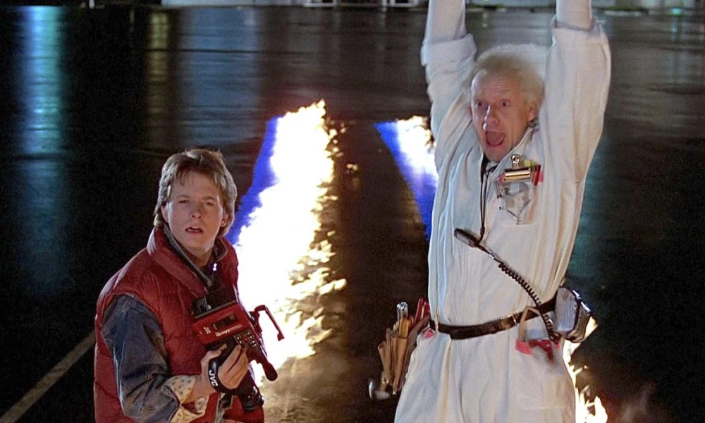 Marty McFly holds a camera while Doc Brown puts his hands in the air in Back to the Future.