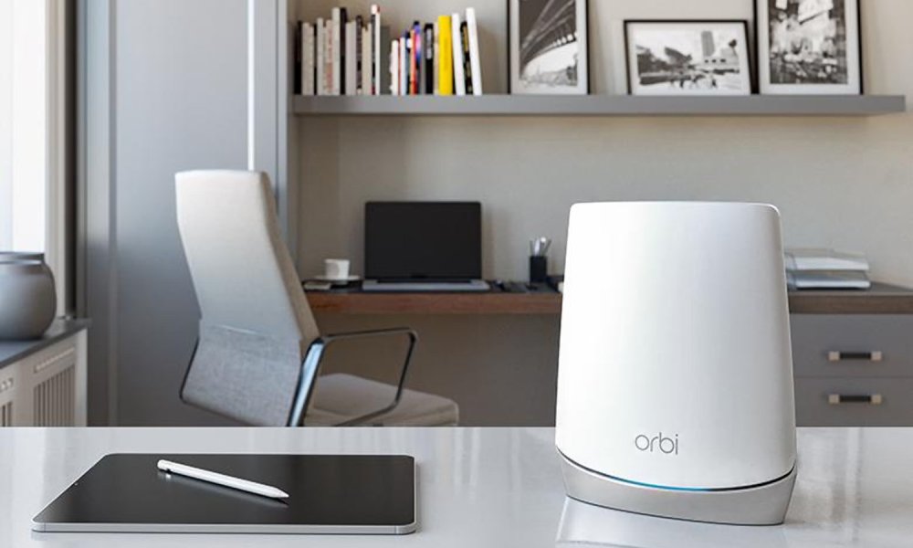 Netgear's Orbi CBR750 sits on a table beside an iPad, with a laptop is in the background.