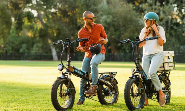 Two people putting on helmets getting ready to ride Lectric XP 3.0 folding e-bikes.