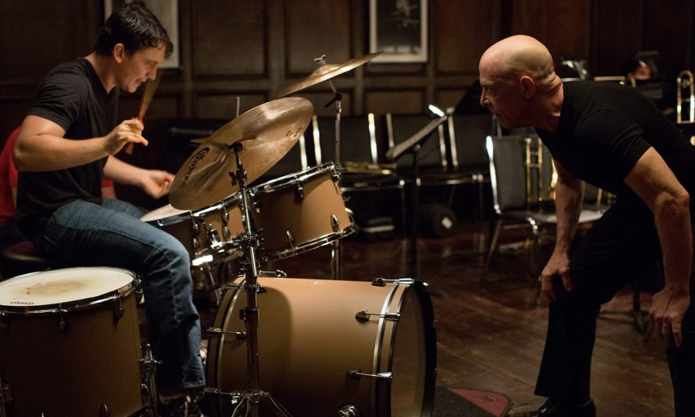 Miles Teller drums while JK Simmons stares in front in Whiplash.