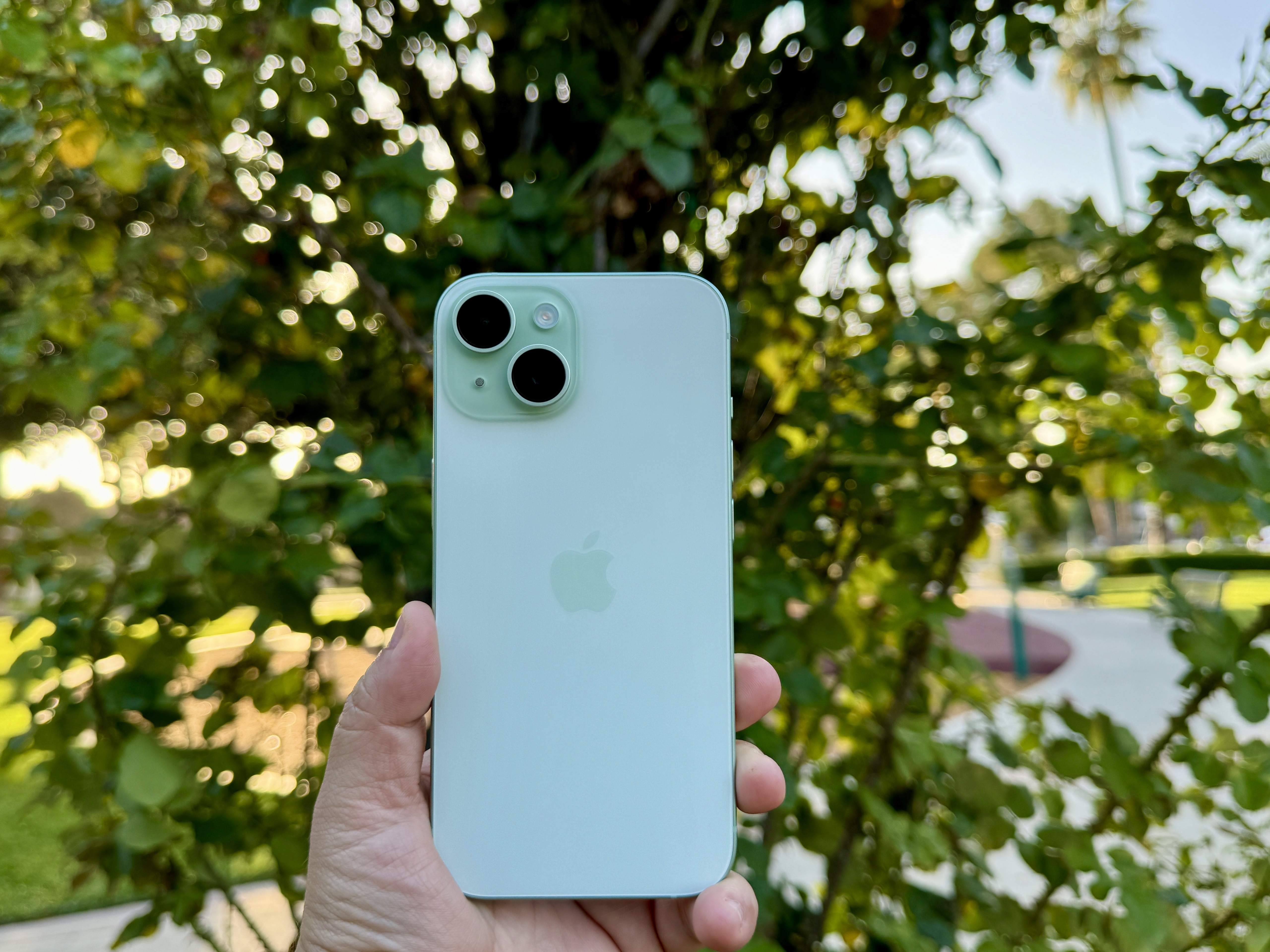 Un iPhone 15 verde en la mano frente a la planta.