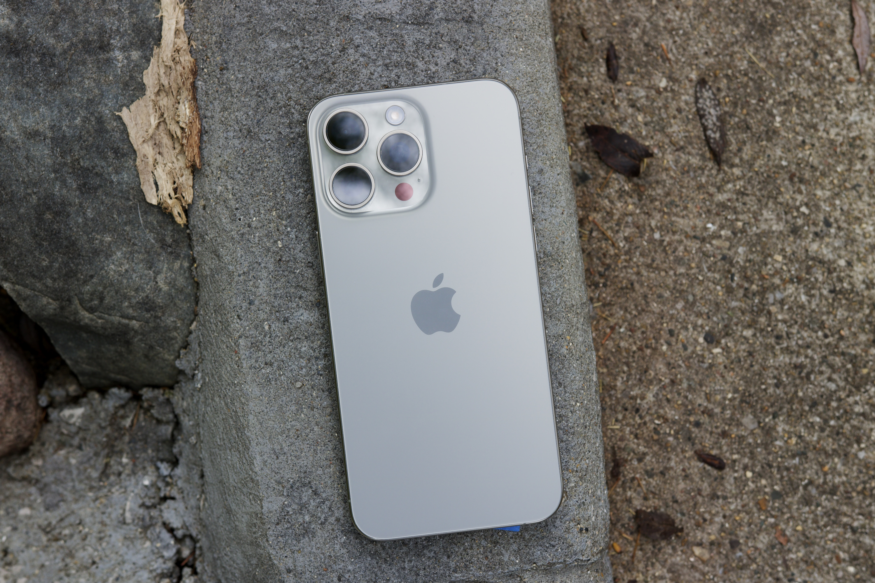 iPhone 15 Pro Max tirado afuera en un parque.