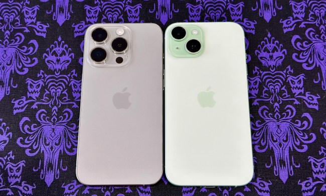 A natural titanium iPhone 15 Pro (left) and a green iPhone 15 on a Haunted Mansion wallpaper placemat.