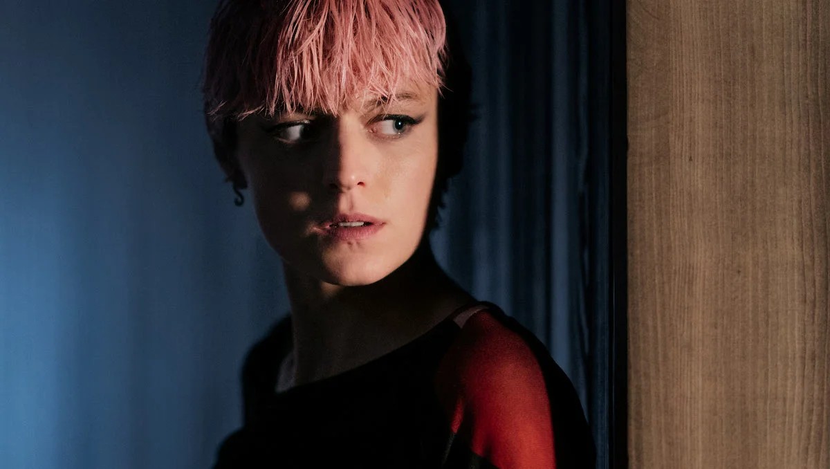 Darby in the dark with pink hair looking suspiciously to her side in a scene from A Murder at the End of the World.