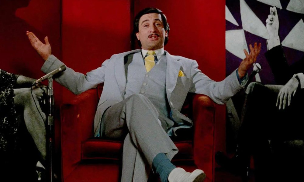 Robert De Niro sits in a red chair in The King of Comedy.