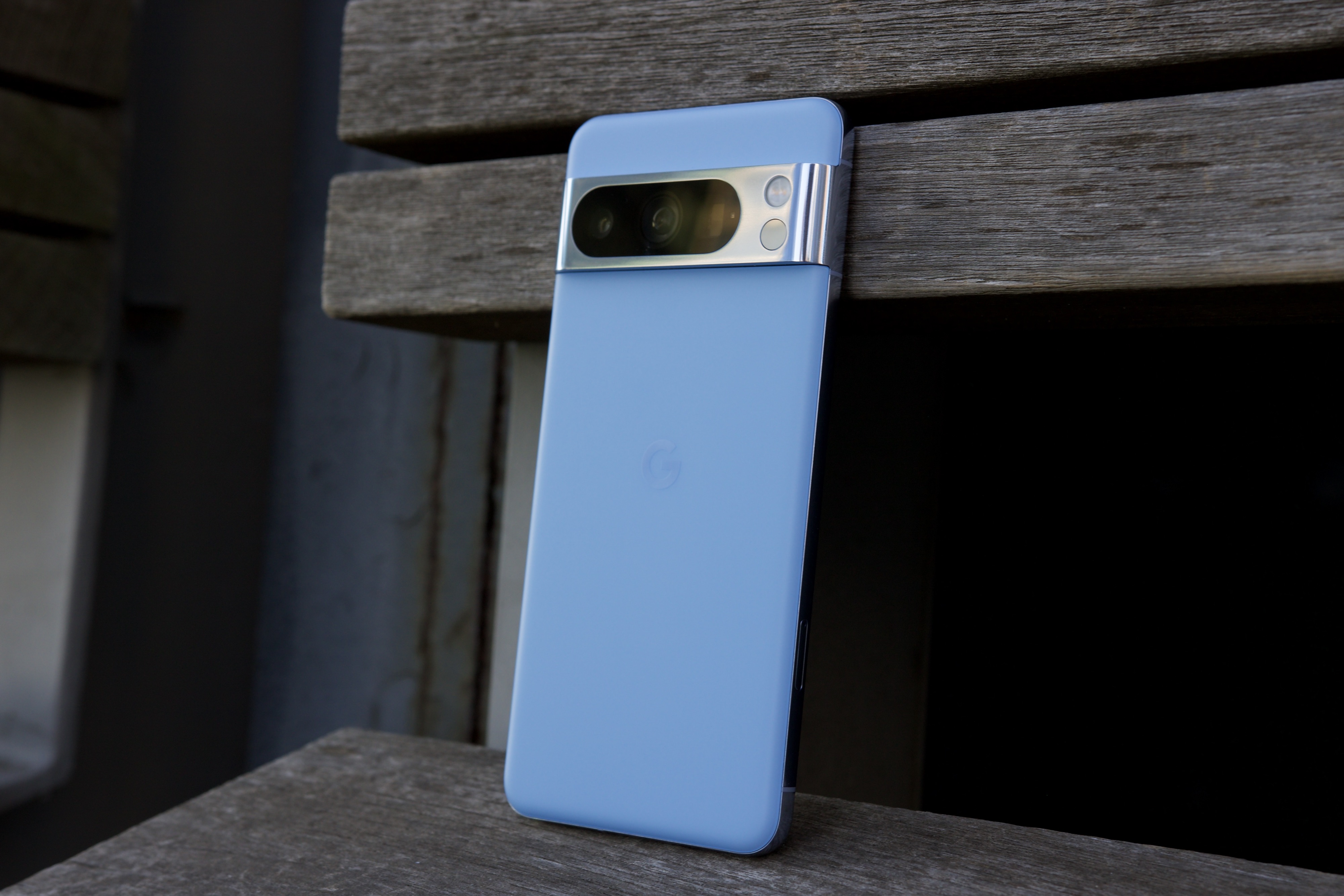 The Google Pixel 8 Pro sitting upright on a park bench.