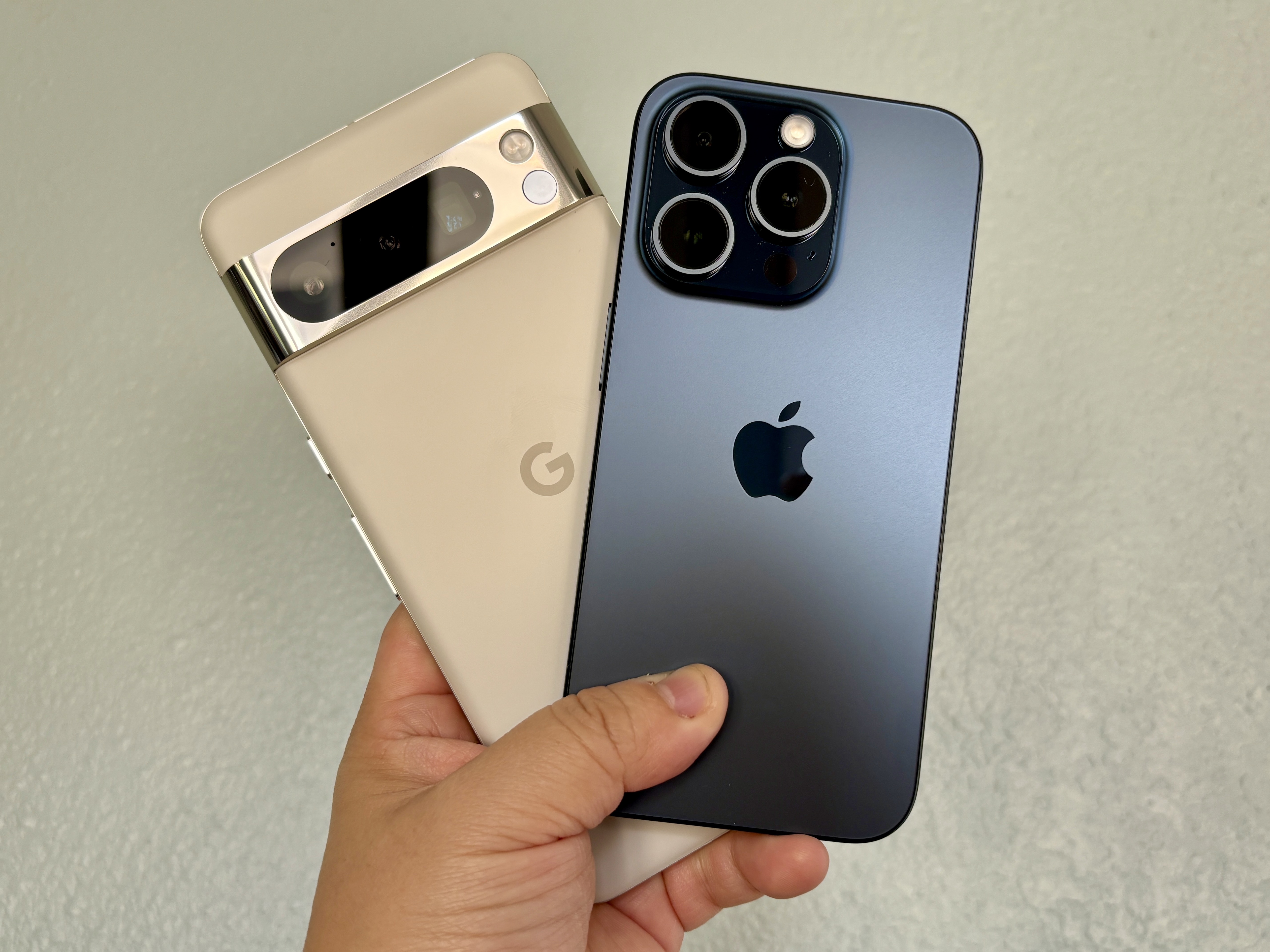 Un Google Pixel 8 Pro en porcelana (izquierda) con un iPhone 15 Pro en azul titanio en la mano.