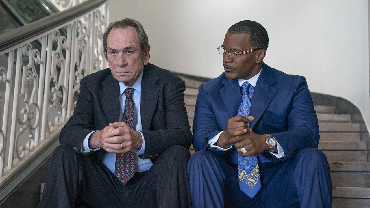 Tommy Lee Jones and Jamie Foxx sitting on steps together in suits in a scene from The Burial.