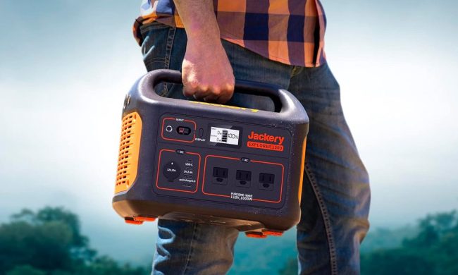 A man carries the Jackery Explorer 1000 portable power station with trees in the background.