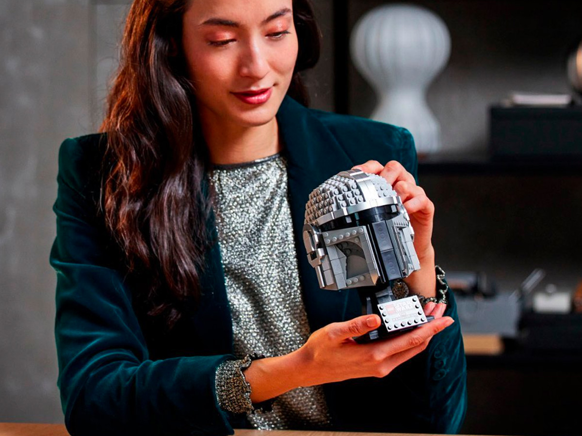 A woman holds at a put together Lego Star Wars The Mandalorian Helmet.