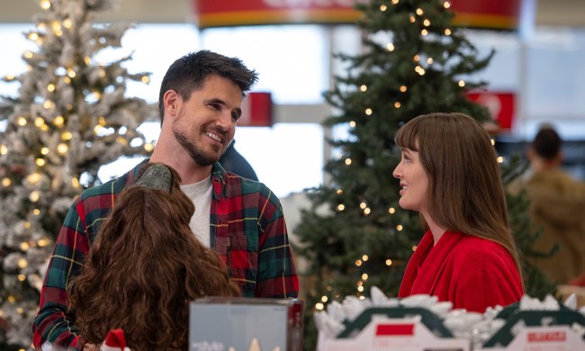 Robbie Amell and Leighton Meester in a festive store looking at one another, smiling in a scene from the movie EXmas.