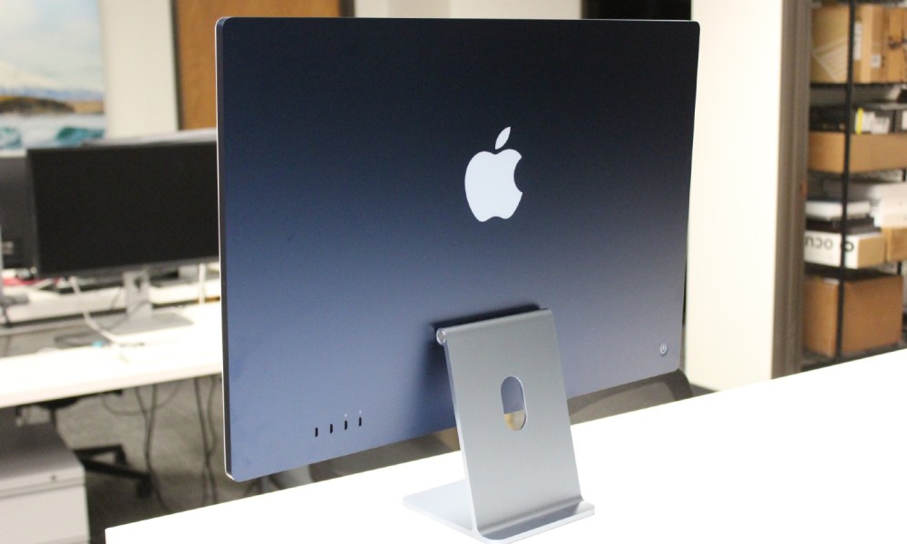 The back of a blue iMac on a white desk.