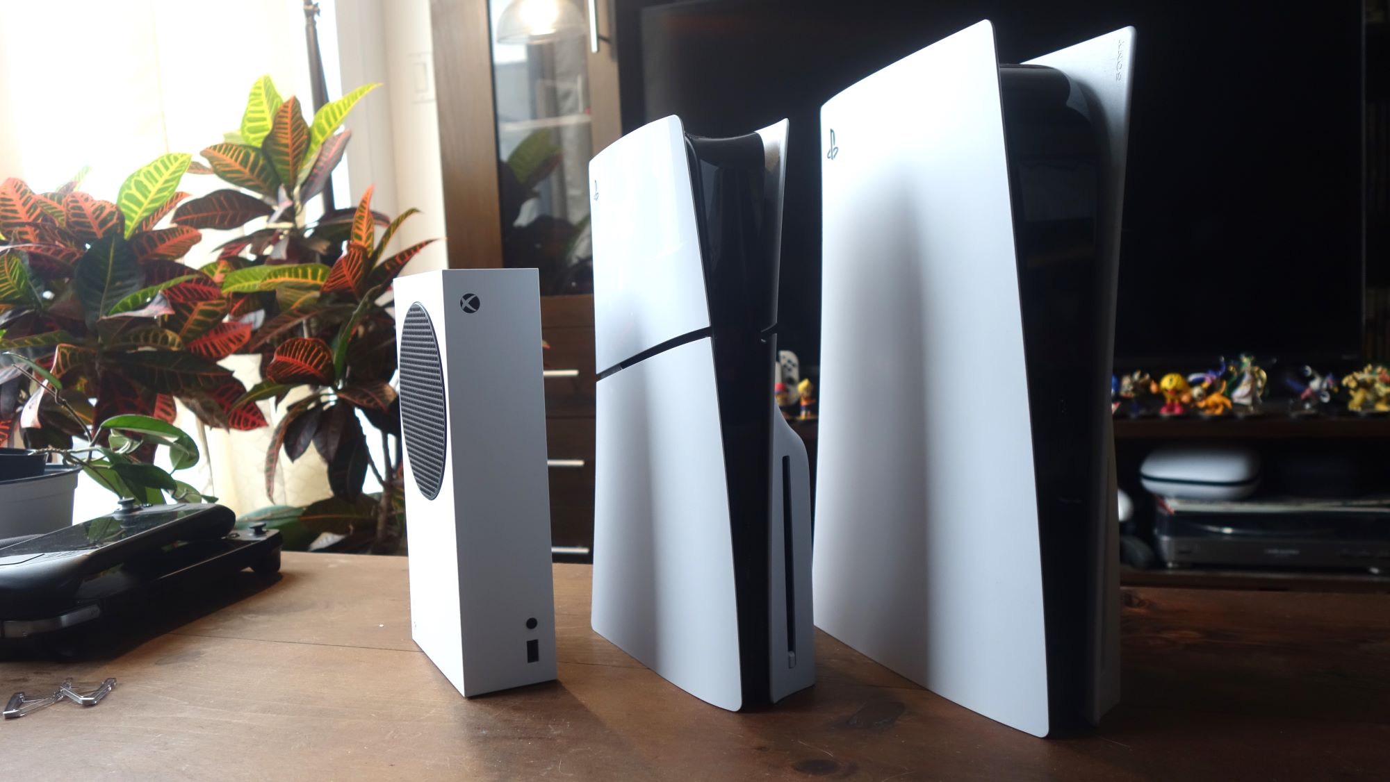 An Xbox Series S, PS5 Slim, and PS5 stand next to one another.
