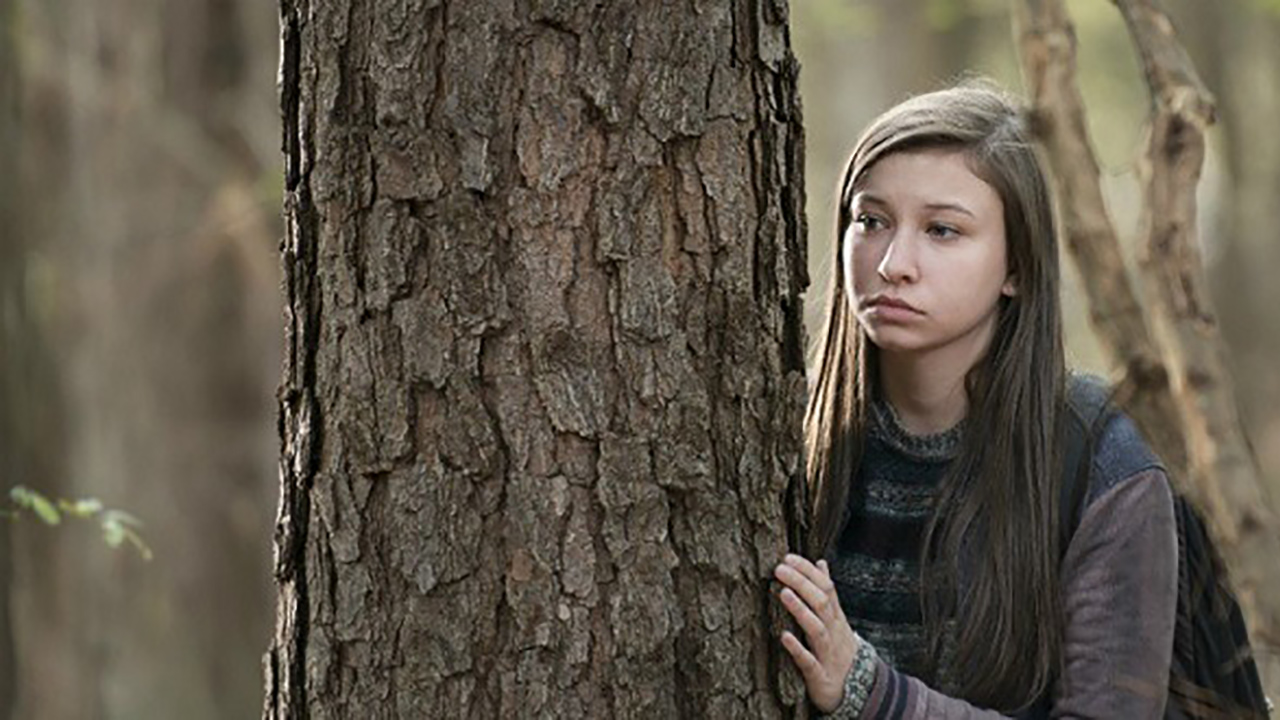 Enid debout derrière un arbre dans une scène de The Walking Dead.