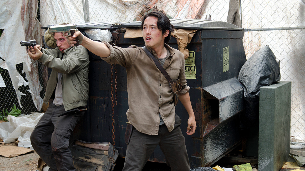 Glenn pointe une arme dans une benne à ordures avec Nicholas derrière lui dans une scène de The Walking Dead.