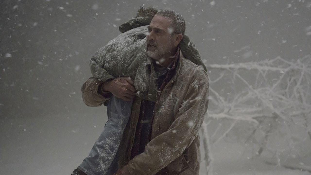 Negan carregando Judith no ombro no meio de uma tempestade de neve em uma cena de The Walking Dead.