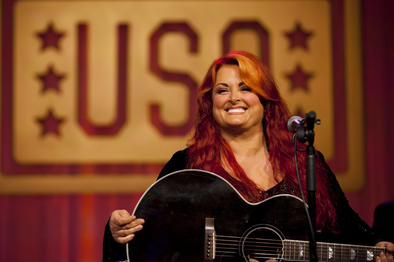 Wynonna Judd holds a guitar and performs a song.