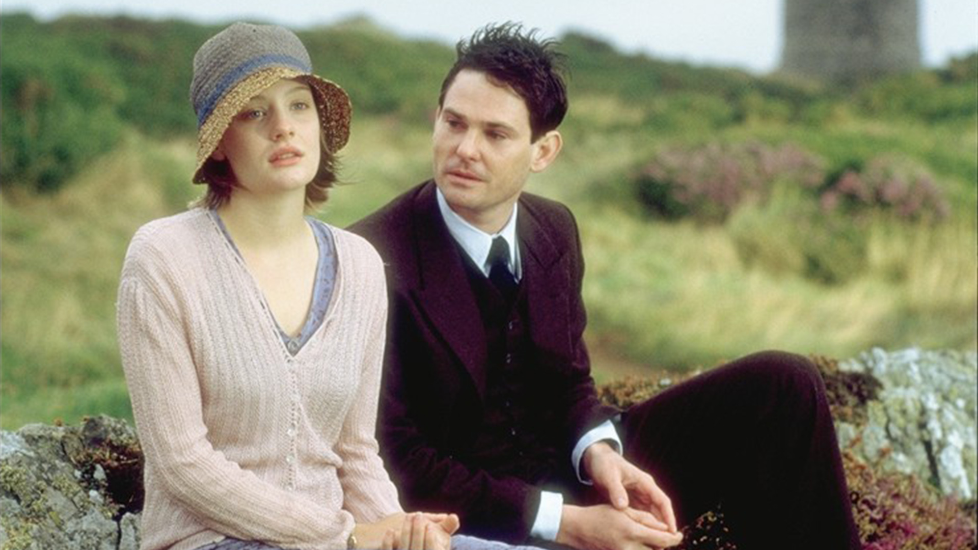 Ramola Garai y Henry Thomas como Cassandra y Simon sentados en un banco al aire libre en Capturo el castillo.